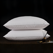 Two white pillows stacked on a dark surface with a small decorative item.